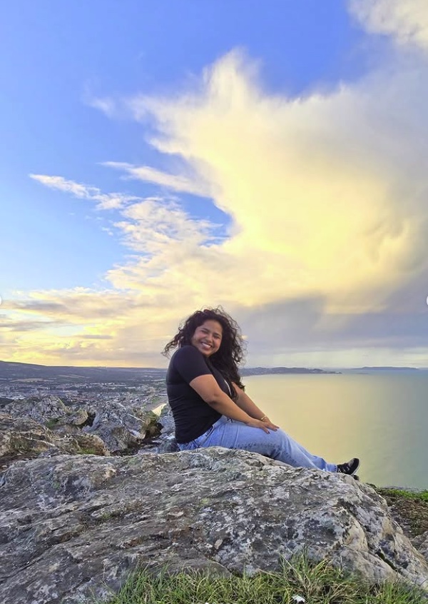 Rosemerry sitting on the rocks at the top of Bray Head, golden clouds over the sea behind her